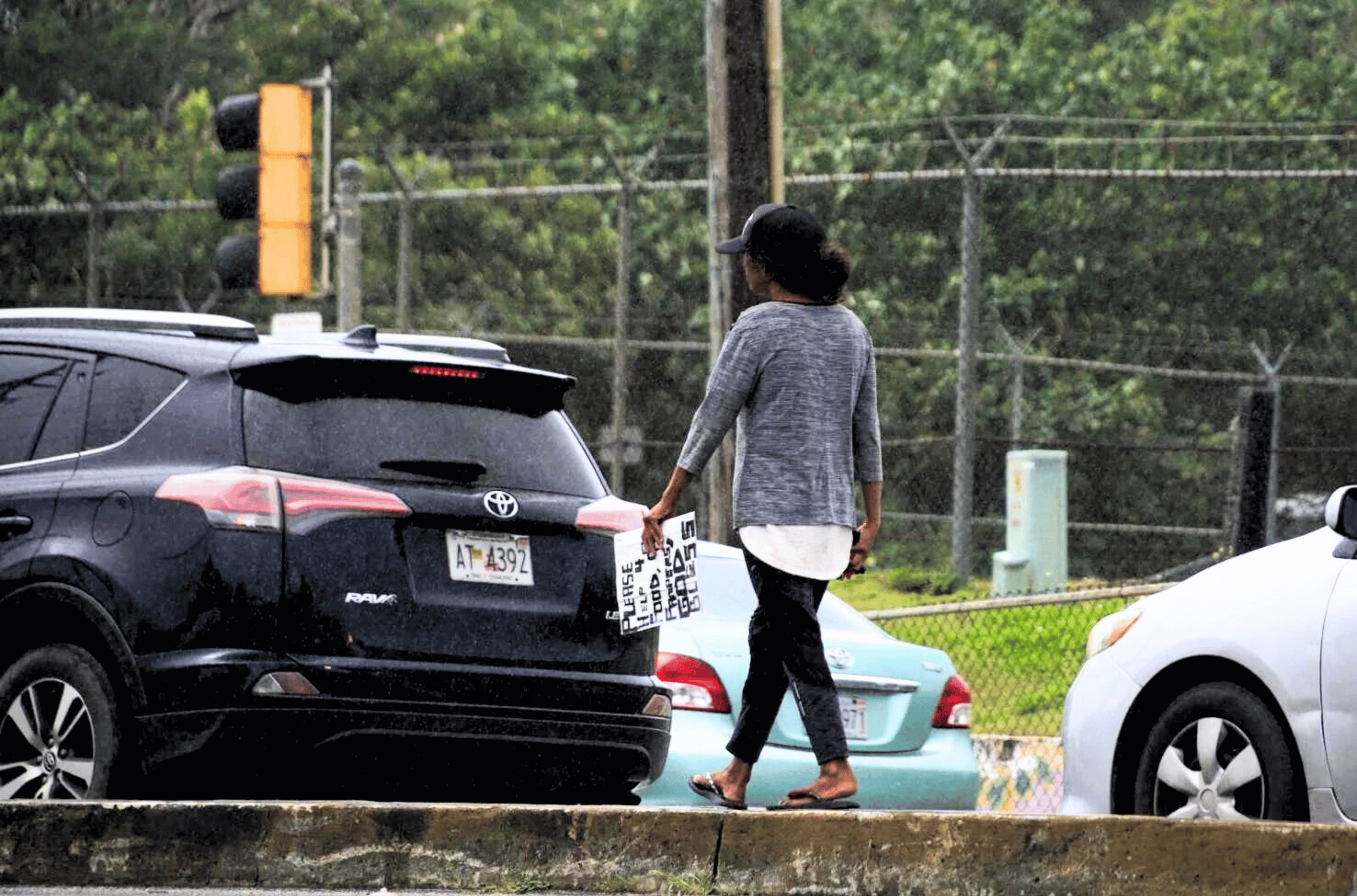 A person holding a sign walks along a Marine Corps Drive median near the Micronesia Mall in Dededo on March 1, 2023. 