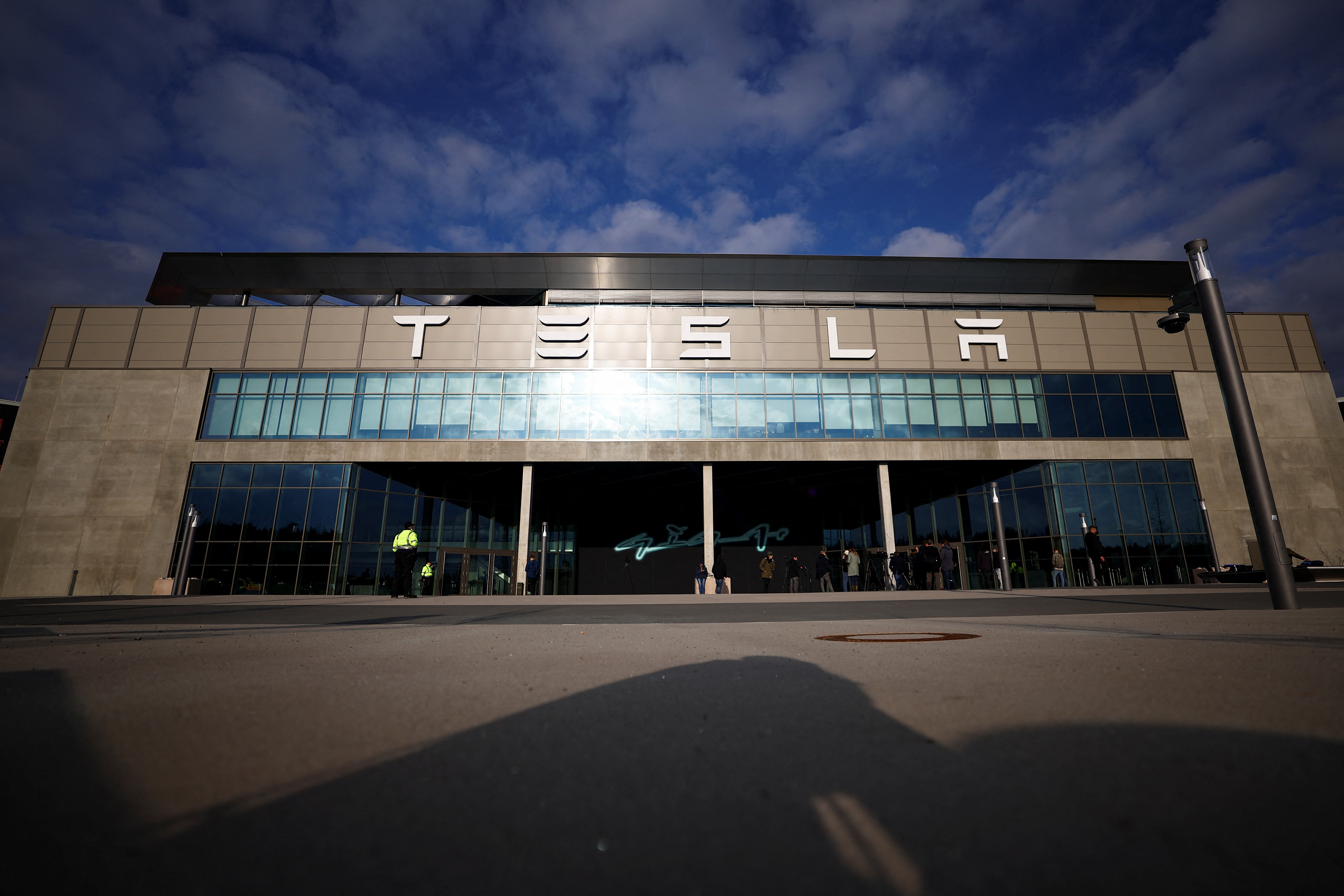 Members of the media stand outside the building of Tesla's production plant in Gruenheide outside Berlin, Germany, March 5, 2024, after the site lost power following a suspected arson attack on a nearby pylon. 