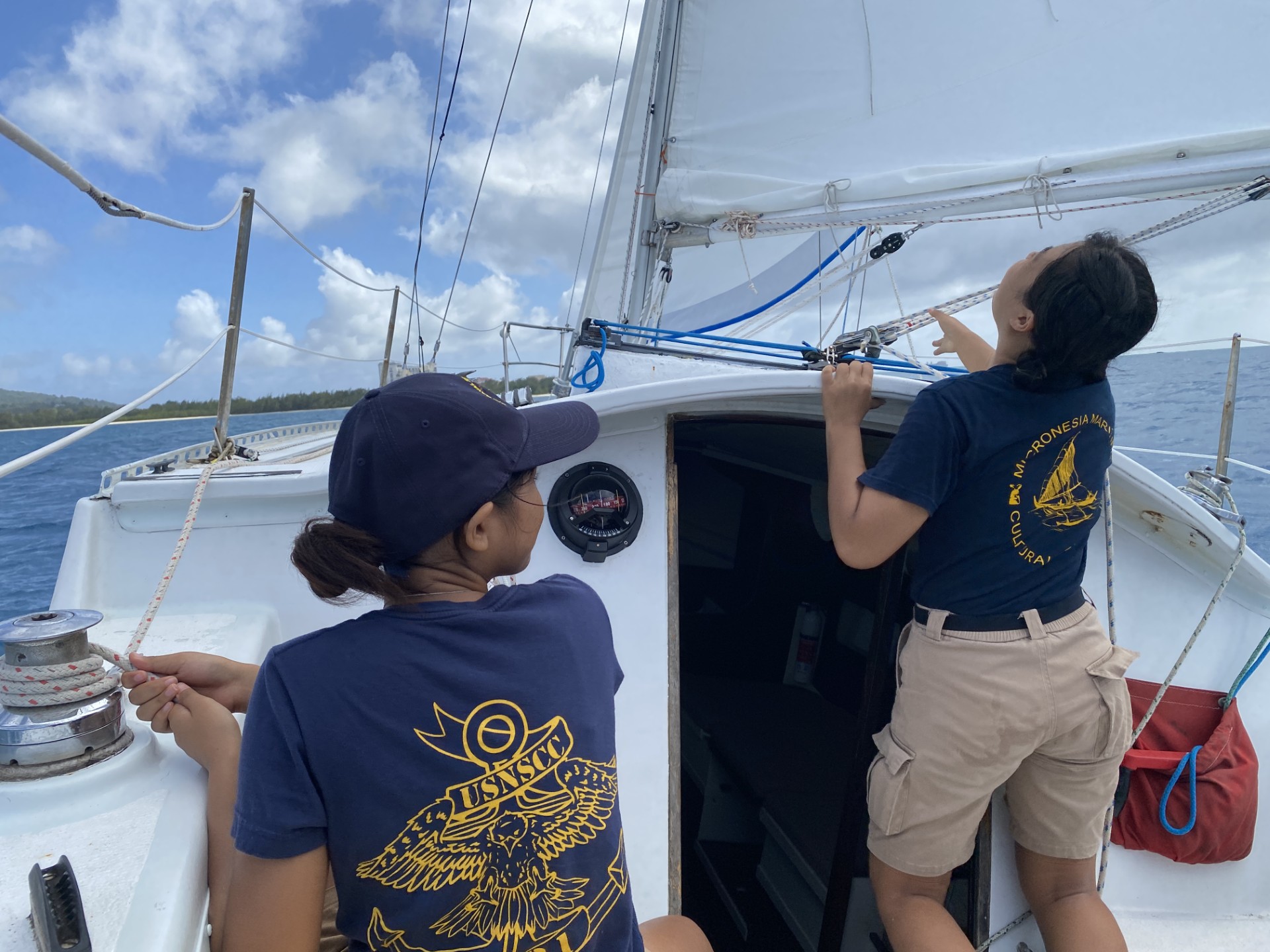 Mary Wang, left, preparers to tighten the line that controls the jib sail, while fellow Sea Cadet Jessica Ma looks up at the mainsail.